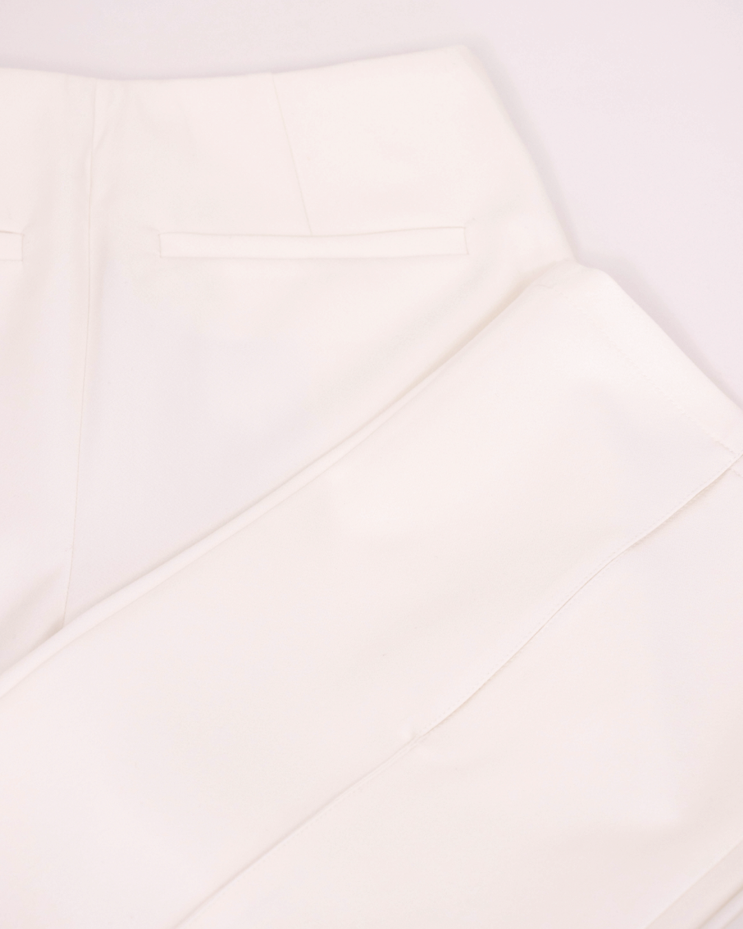 Fitted white tailored trousers with a sleek, sculpted fit and front slits. Back pocket detailing, structured waistband, and precise tailoring for an elevated look – BOLDNSUBTLE.
