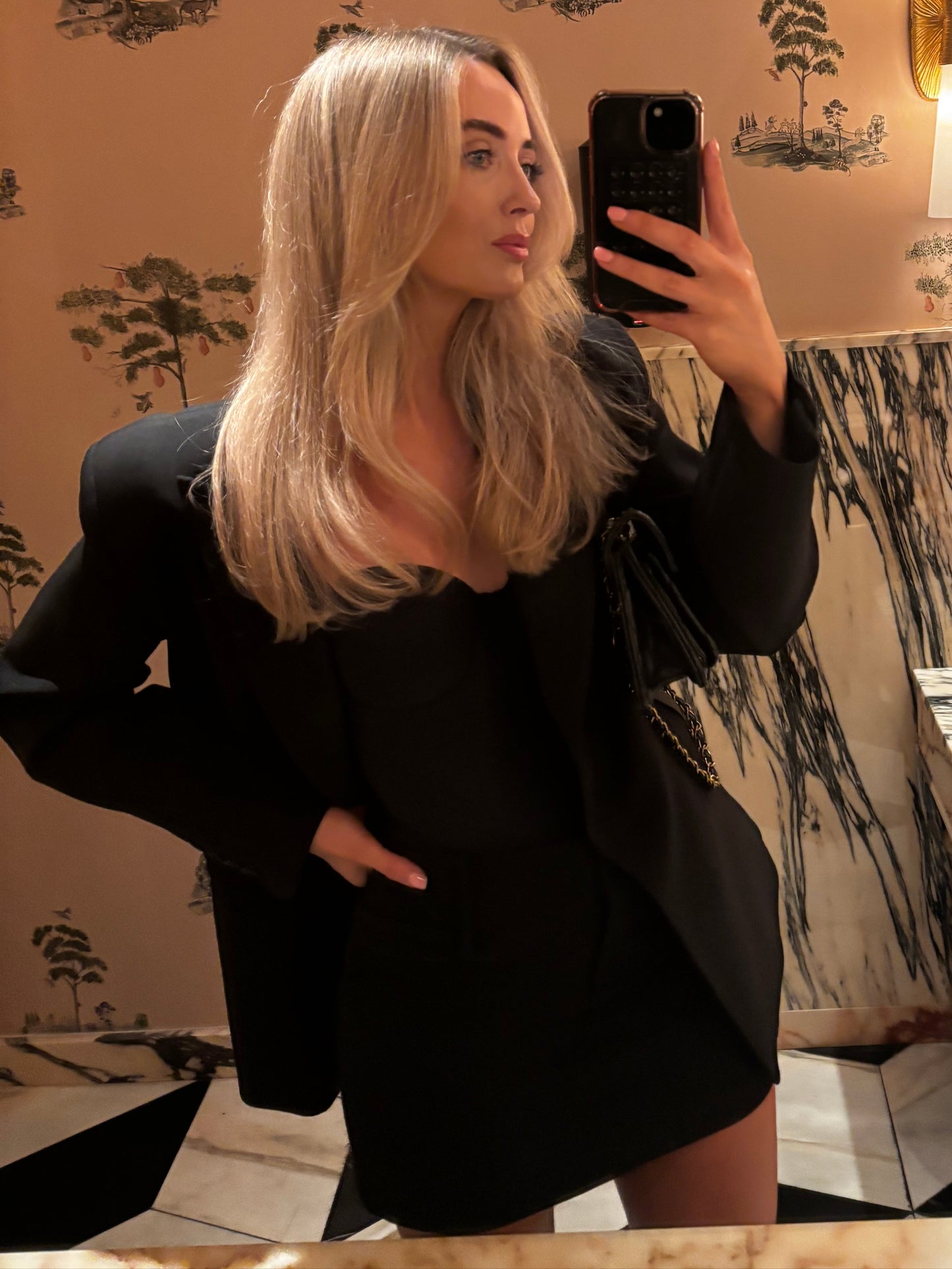 Person taking a mirror selfie with floral wallpaper in the background