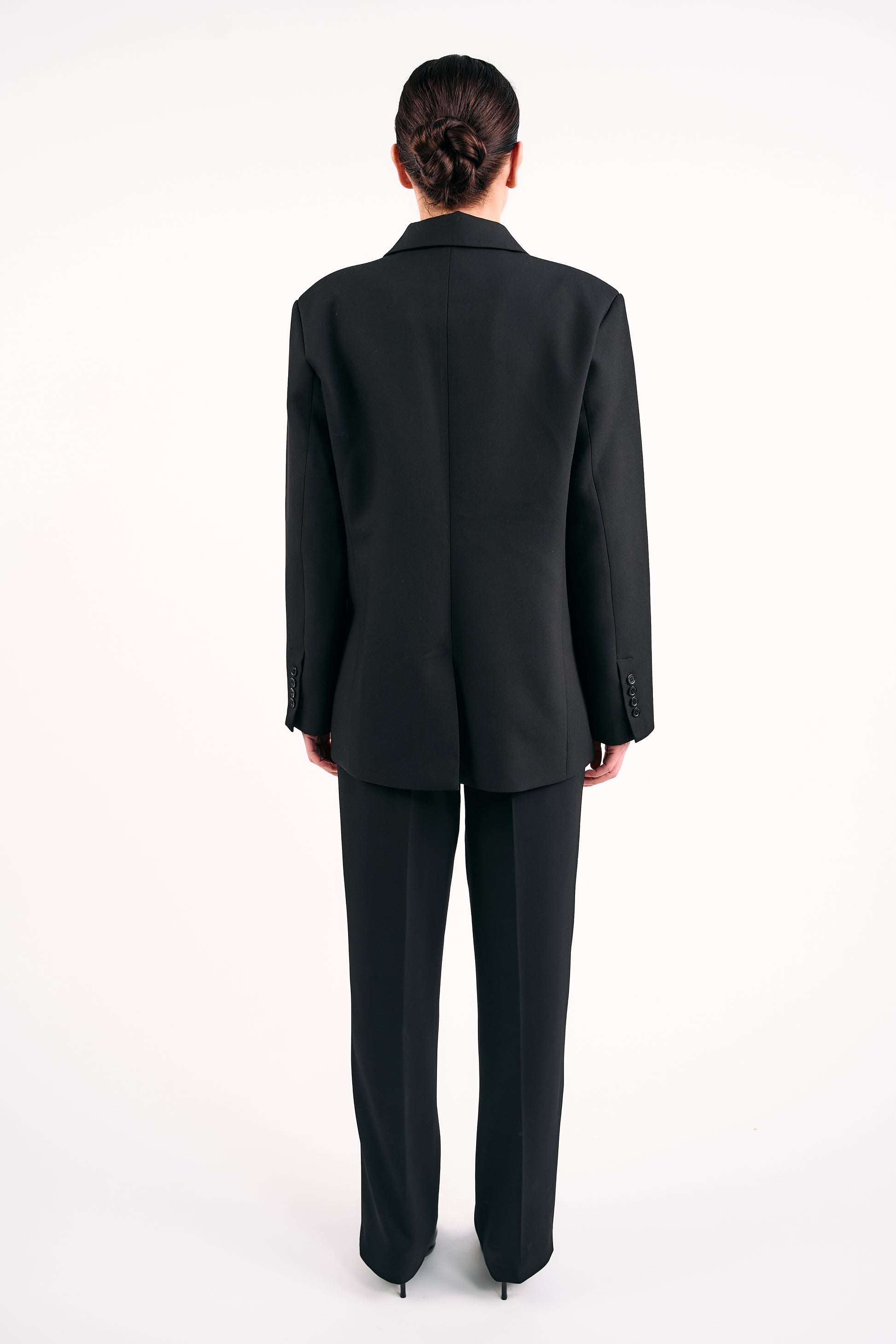 Back view of model wearing BOLDNSUBTLE’s Black Blazer made in Ireland with tailored trousers against a white background.