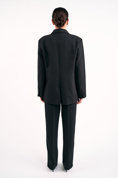 Back view of model wearing BOLDNSUBTLE’s Black Blazer made in Ireland with tailored trousers against a white background.