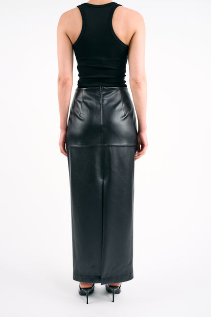 Black high-waisted PU maxi skirt styled with a fitted black tank top and pointed heels, photographed against a white background in a minimalist studio setting.