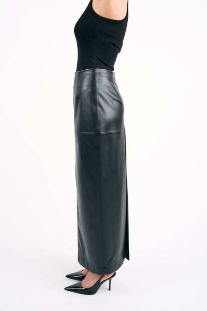 Woman wearing a black PU leather maxi skirt with a side slit and a black sleeveless top, photographed from the side against a white background.