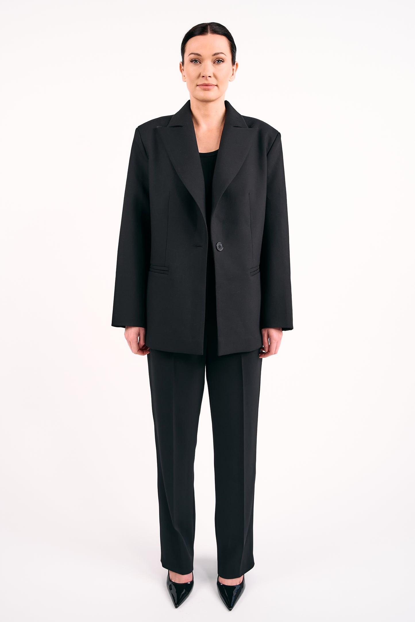 Woman wearing a black tailored blazer and matching black trousers against a white background.